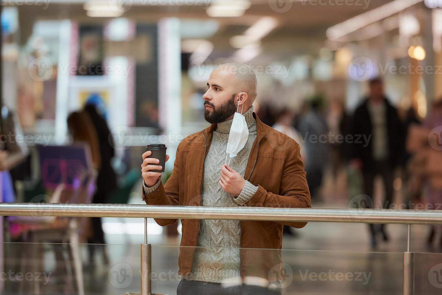 Ein Mann hält eine abgenommene Maske in der Hand, während er im Einkaufszentrum Kaffee trinkt foto