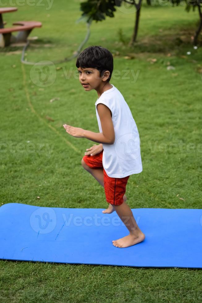 asiatisch Clever Kind tun Yoga Pose im das Gesellschaft Park draussen, Kinder- Yoga Pose. das wenig Junge tun Yoga Übung. foto