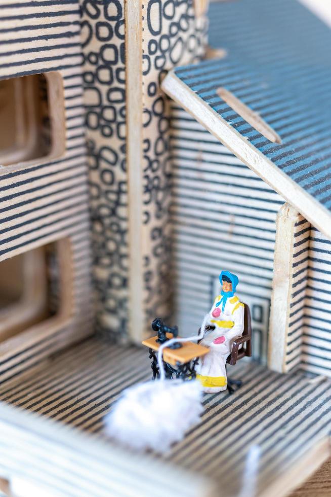 Miniaturmenschen, Frau, die an einer Nähmaschine in ihrem Haus näht. weibliche Näherin, die an einer Nähmaschine arbeitet foto
