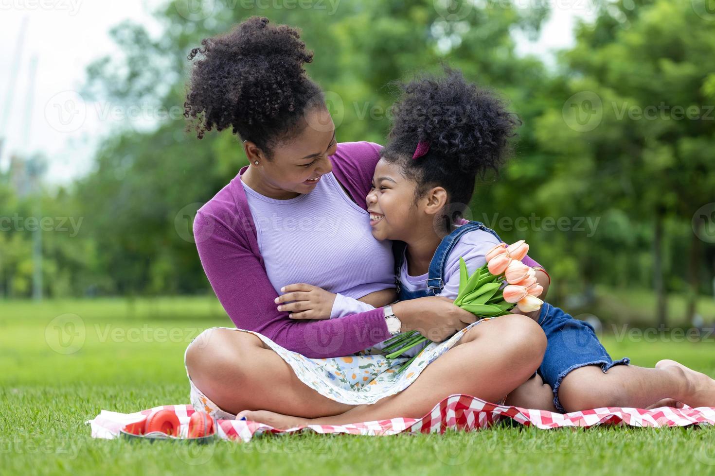 afrikanisch Mutter halten Strauß von Tulpe Blumen und das Tochter umarmen jeder andere während glücklich genießen Picknick im das Öffentlichkeit Park während Sommer- zum Familie Liebe und Pflege im Mutter Tag Feier foto