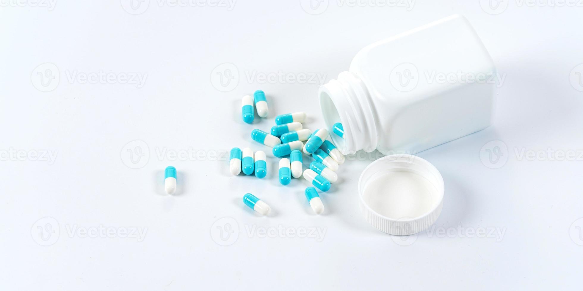 blaue und weiße Kapseltabletten, die aus der Flasche auf weißem Hintergrund gießen foto