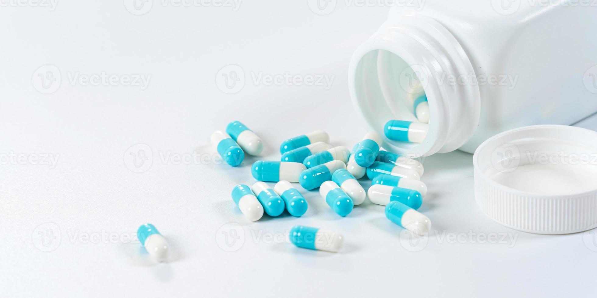 blaue und weiße Kapseltabletten, die aus der Flasche auf weißem Hintergrund gießen foto