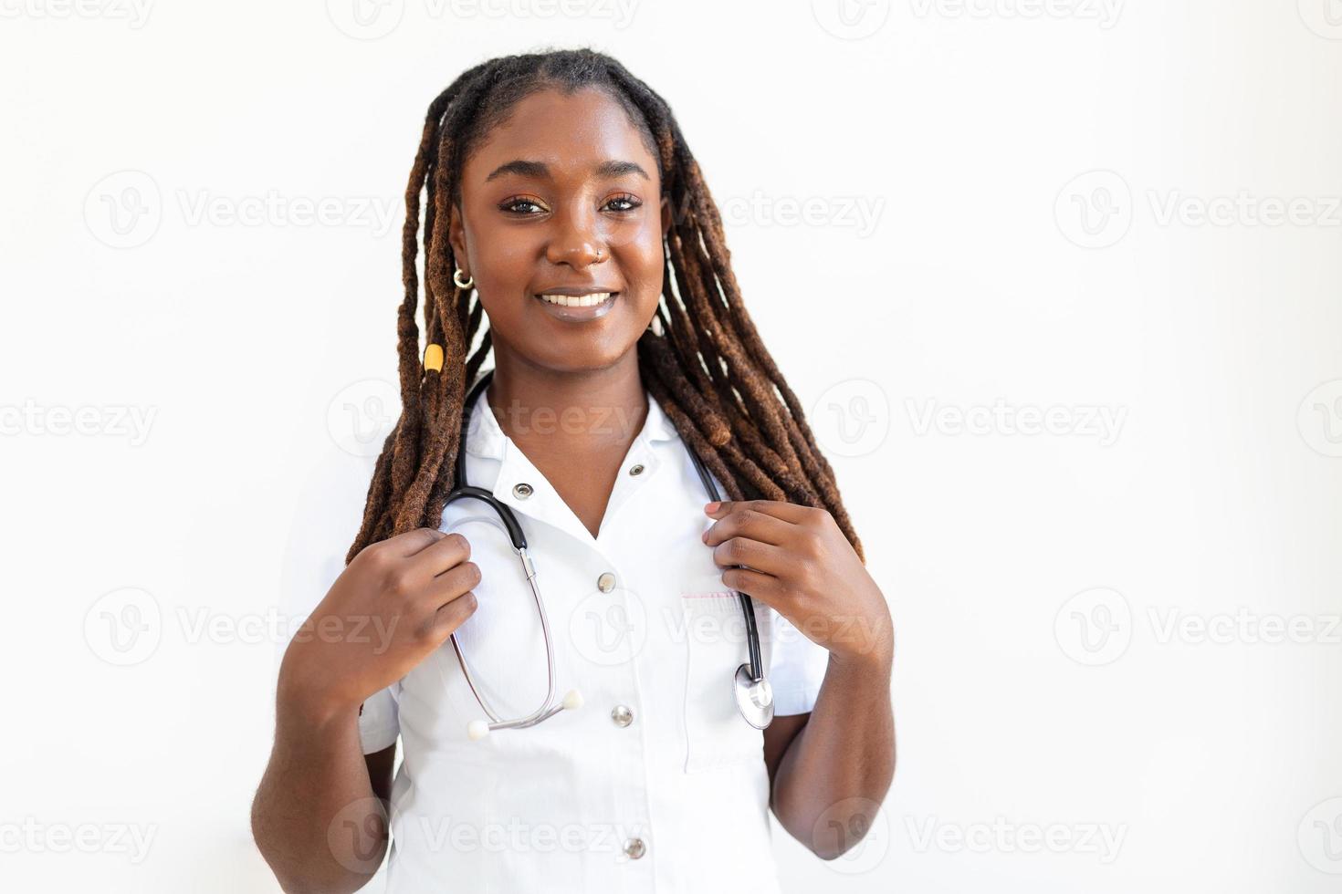 Zuversichtlich lächelnde Ärztin posiert und blickt mit Stethoskop in den Händen in die Kamera. freundliche afroamerikanerärztin lächelnd. Arzt mit Stethoskop um den Hals foto
