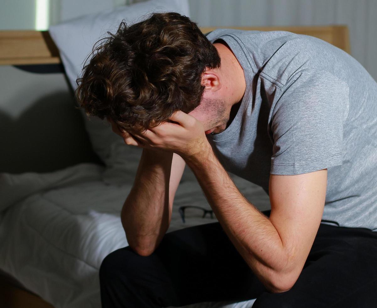 Mann sitzt im Schlafzimmer gestresst wegen Arbeitslosigkeit foto