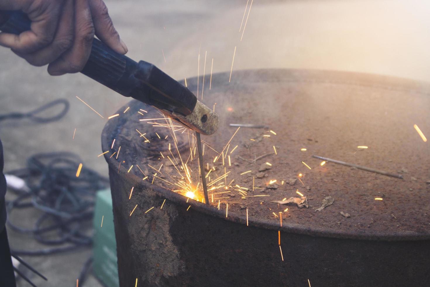 Der Arbeiter der technischen Industrie schweißt Eisenstücktank bei der Arbeit mit einem Funkenblitzlicht foto