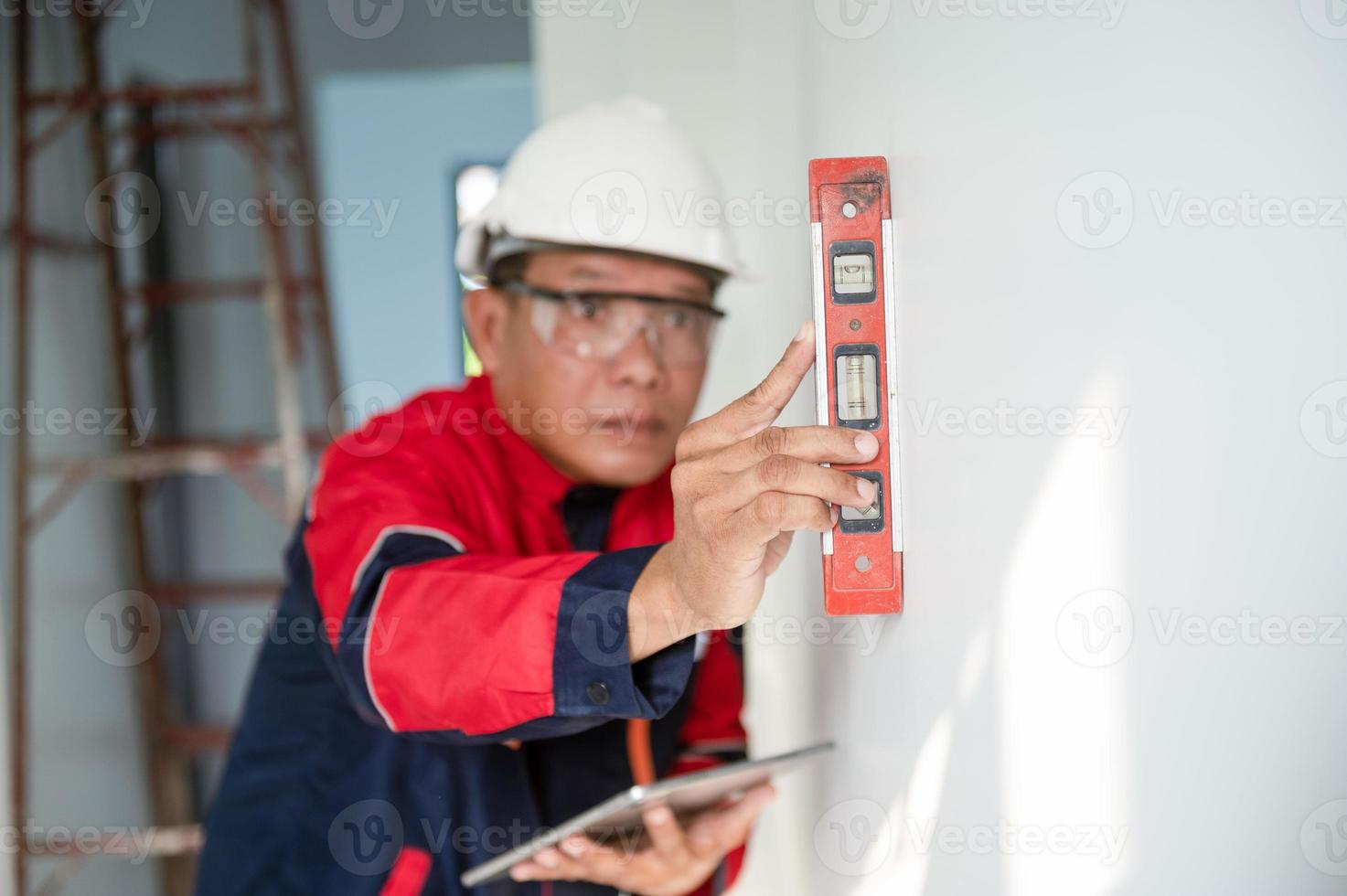 ein Konstruktion Arbeiter oder Architekt tragen ein schwer Hut ist Überprüfung das Mauer mit ein Niveau Messgerät. foto
