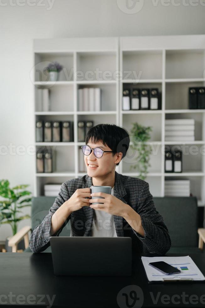 asiatisch Geschäft Mann sind Erfreut und glücklich mit das Arbeit Sie tun auf ihr Tablette, Laptop und nehmen Anmerkungen beim das Büro. foto