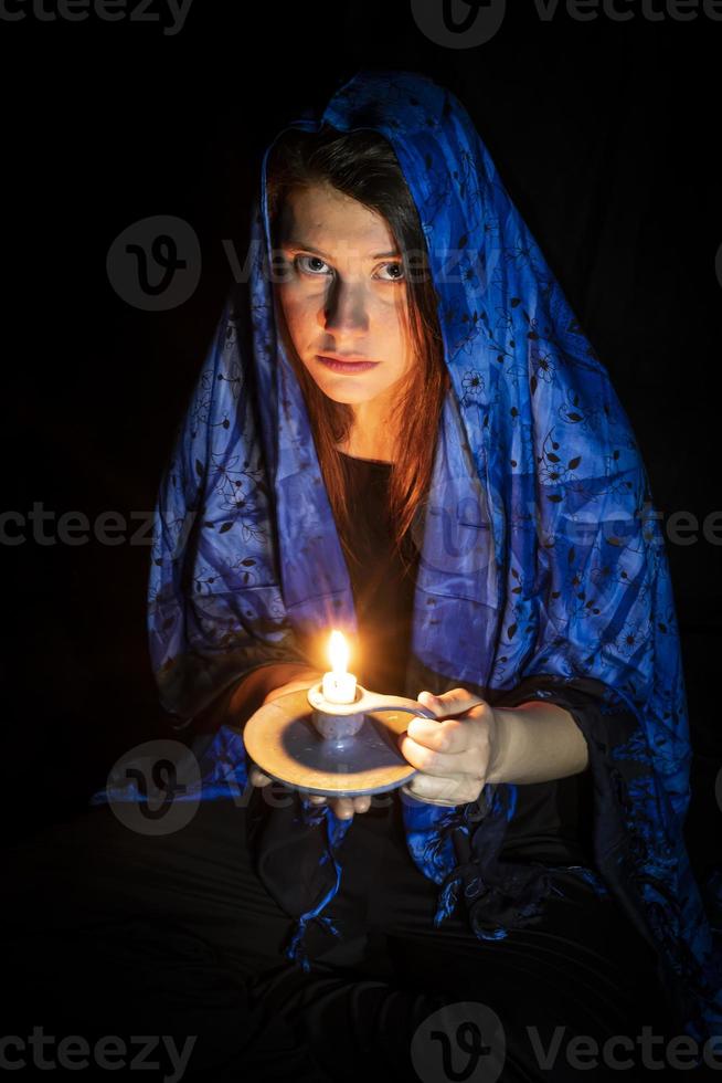 traurige junge Frau mit Kerze und blauem Kopftuch foto