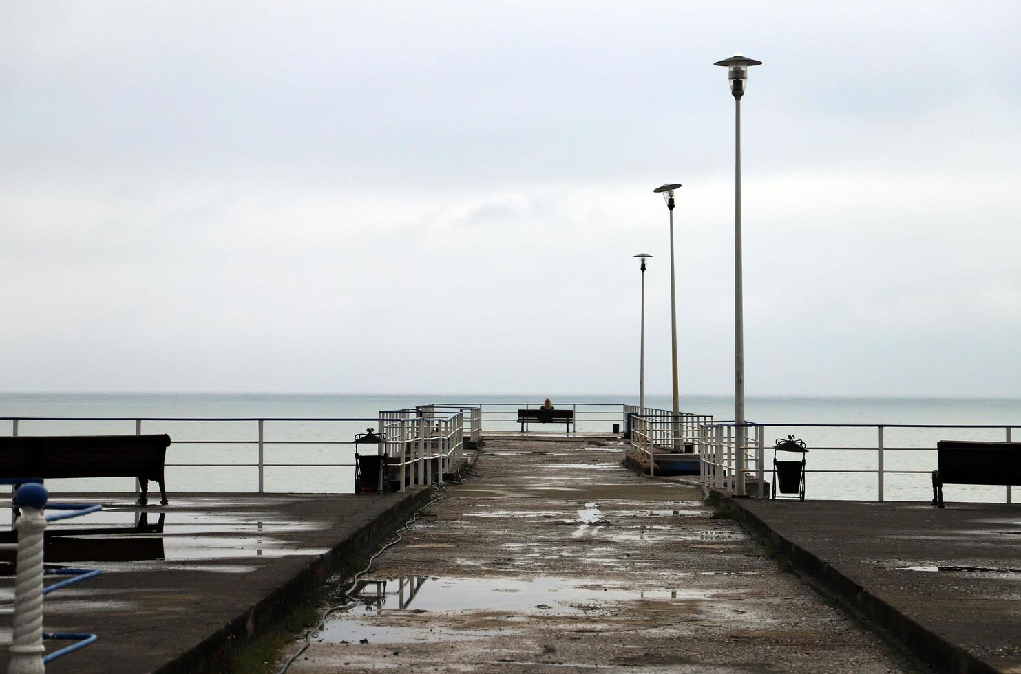 silhoutte von ein einsam Mädchen Sitzung auf ein Bank auf das Seebrücke und suchen beim das Meer im wolkig Wetter. foto