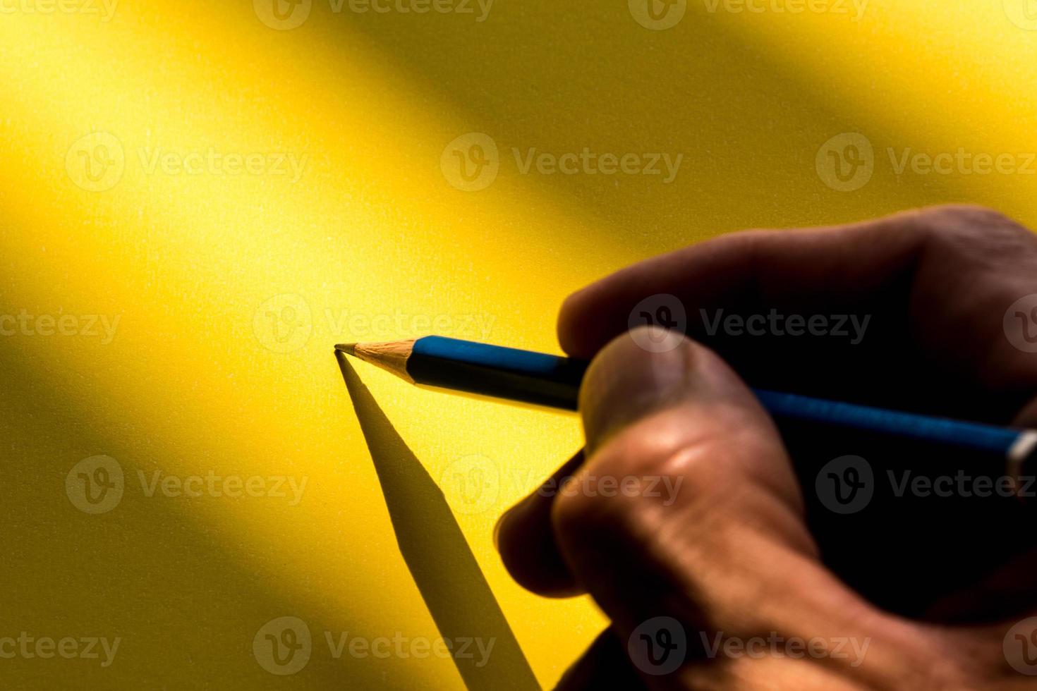 die Hand des Menschen, die einen Bleistift hält, um im Schatten auf das Papier zu schreiben foto