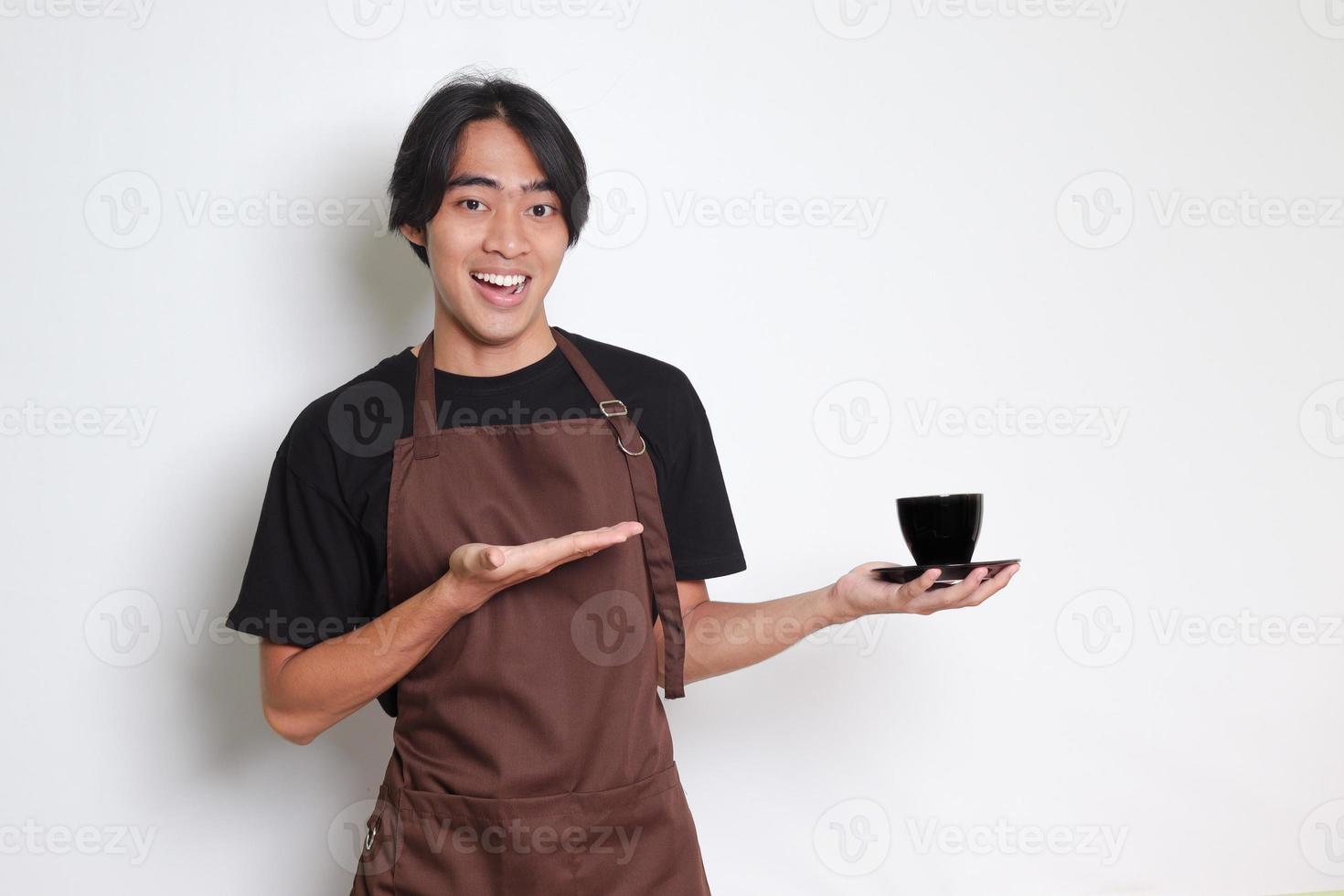 Porträt von attraktiv asiatisch Barista Mann im braun Schürze Portion ein Tasse von Kaffee zu das Kunde. isoliert Bild auf Weiß Hintergrund foto