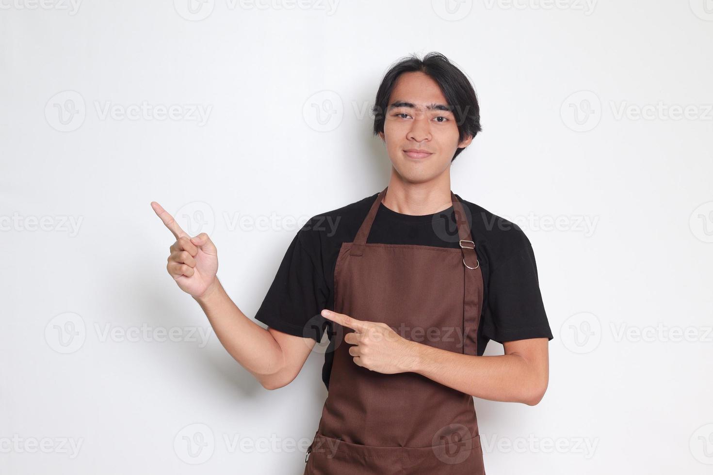 Porträt von attraktiv asiatisch Barista Mann im braun Schürze zeigen Produkt, zeigen beim etwas mit Hände. Werbung Konzept. isoliert Bild auf Weiß Hintergrund foto
