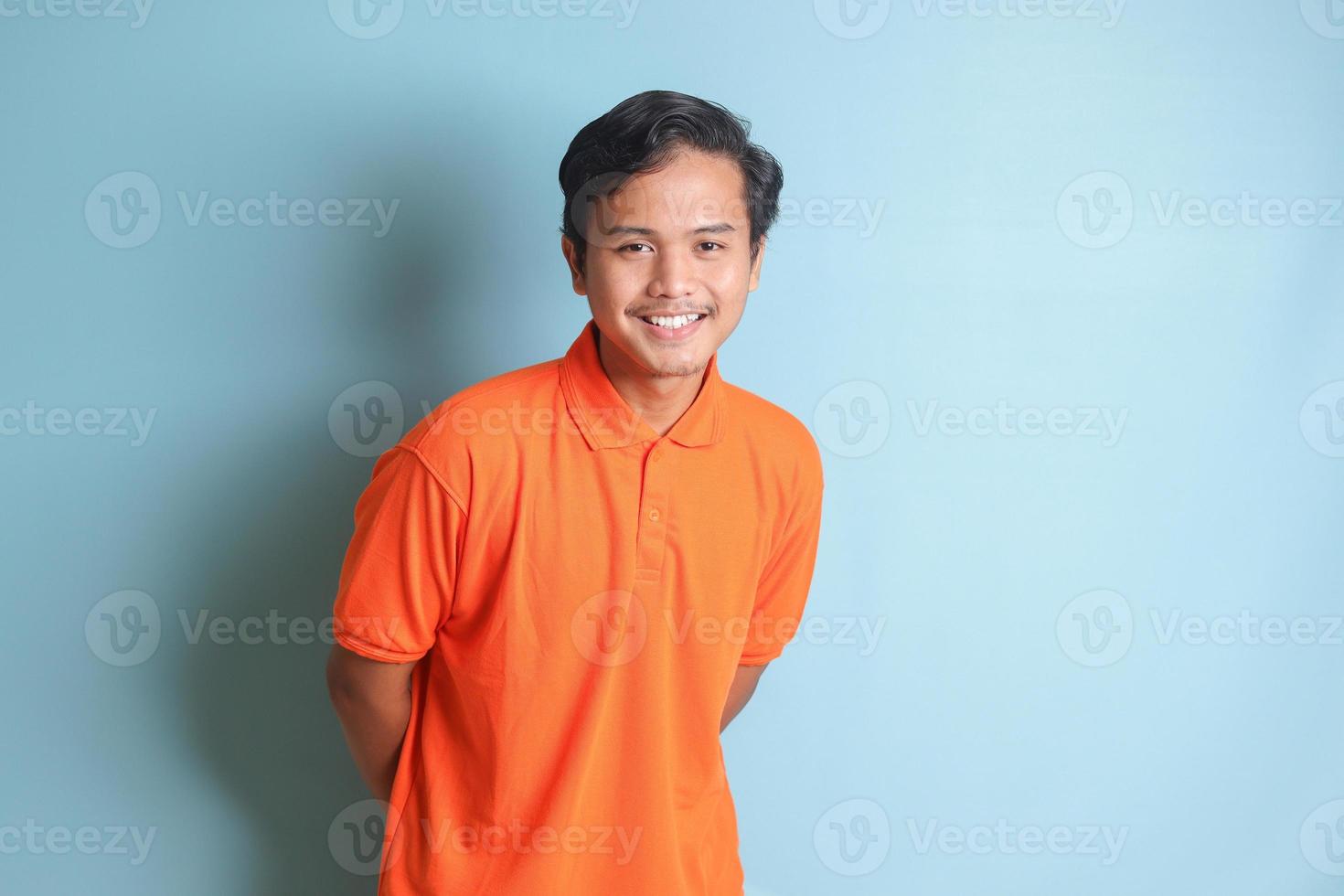 attraktiv asiatisch Mann im Orange Hemd suchen beim Kamera und Gefühl zuversichtlich. isoliert Bild auf Blau Hintergrund foto