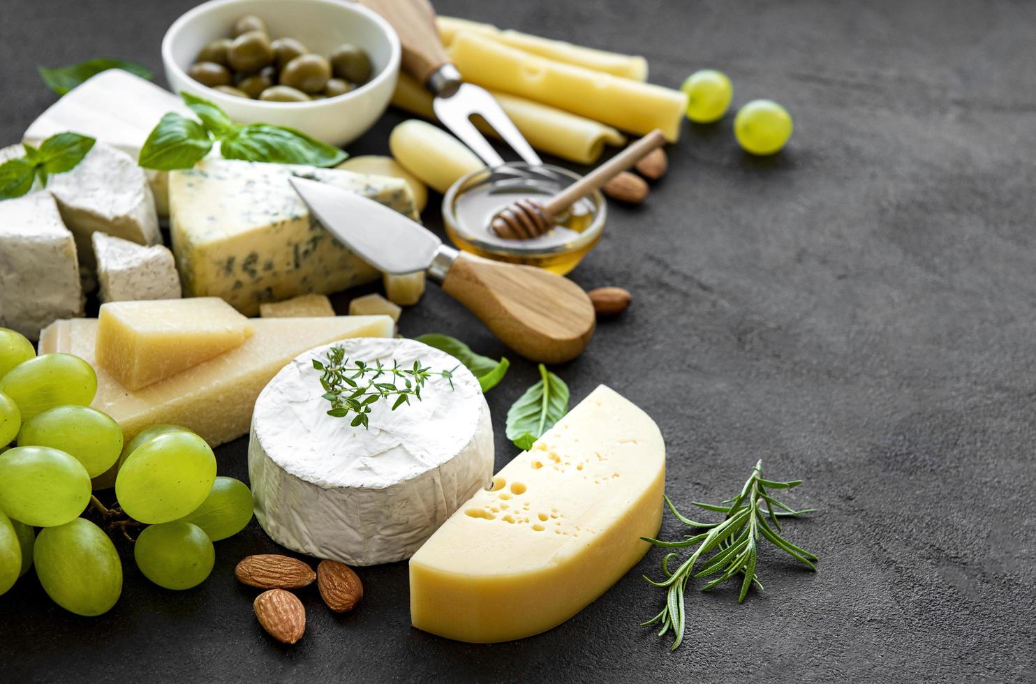 verschiedene Arten von Käse, Trauben, Honig und Snacks auf einem schwarzen Betonhintergrund foto