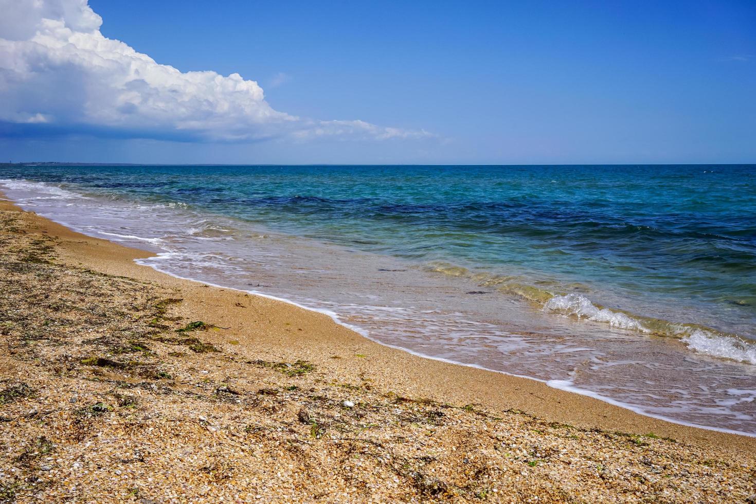 Sand- und Muschelstrand des Meeres in der Krim auf dem Hintergrund des hellen blauen Meeres und des klaren Himmels foto