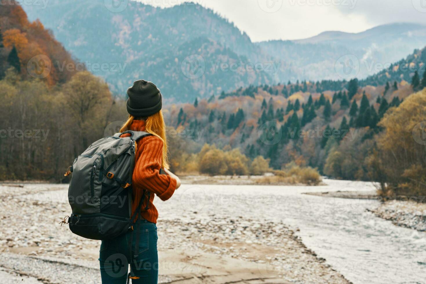 ein Reisender mit ein Rucksack im ein Sweatshirt und Jeans sind ruhen im das Berge im Natur in der Nähe von das Fluss im Herbst foto