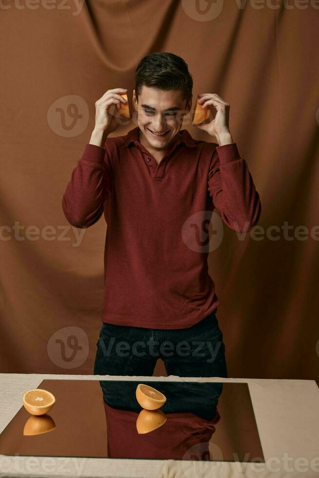 ein Mann im ein rot Hemd mit Orangen im seine Hände ein Spiegel auf das Tabelle foto