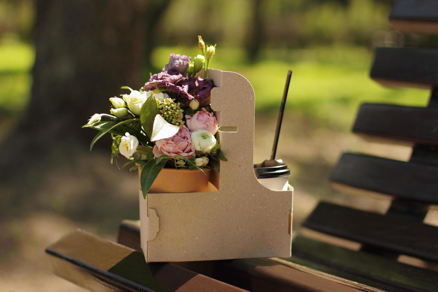 Blumenstrauß und Kaffee zum Mitnehmen auf einer Parkbank foto