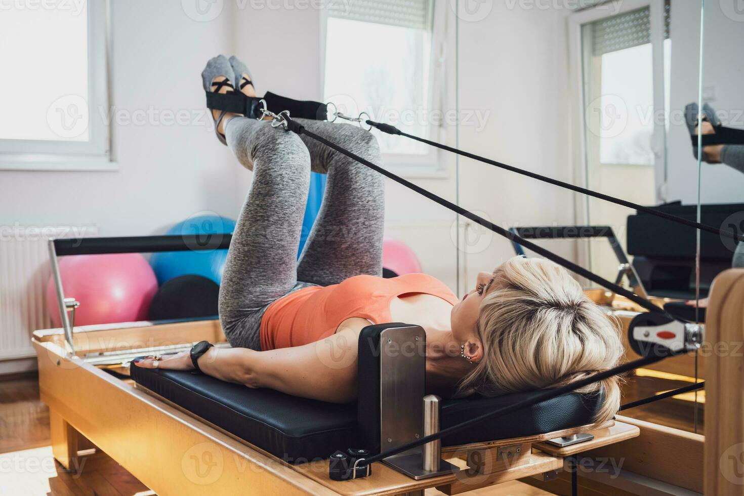 blond Frau ist ausüben auf Pilates Reformer Bett im ihr heim. foto