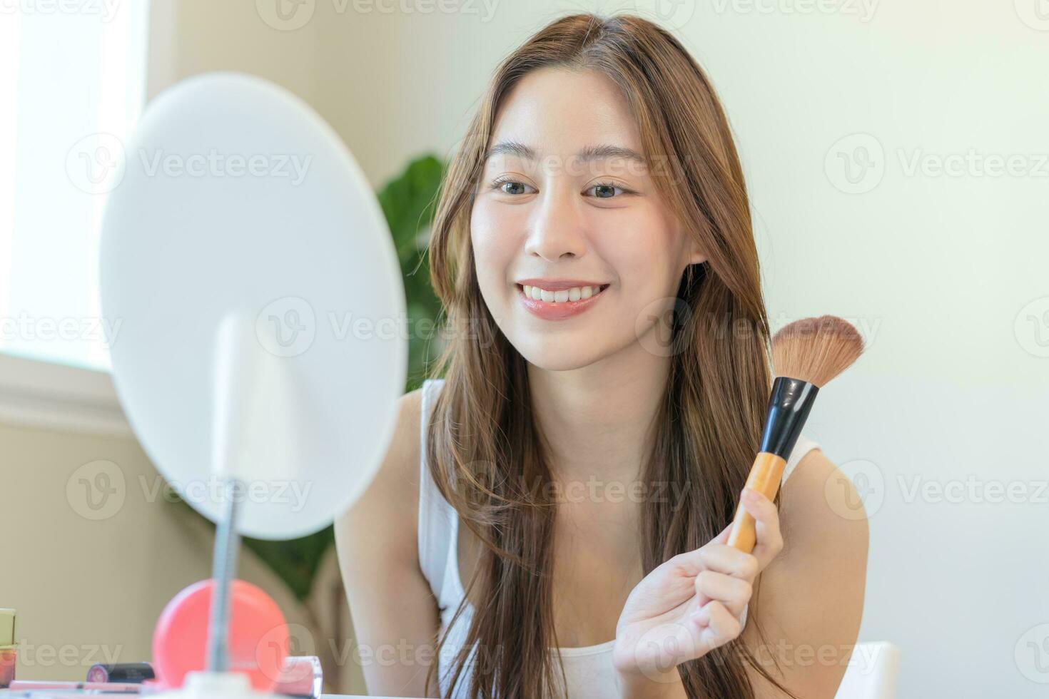 glücklich Routine Schönheit Konzept, ziemlich asiatisch jung Frau, Mädchen machen oben Gesicht durch bewirbt sich Pulver Stiftung durch Bürste um Gesicht, suchen beim das Spiegel beim heim. weiblich aussehen mit natürlich Mode Stil. foto