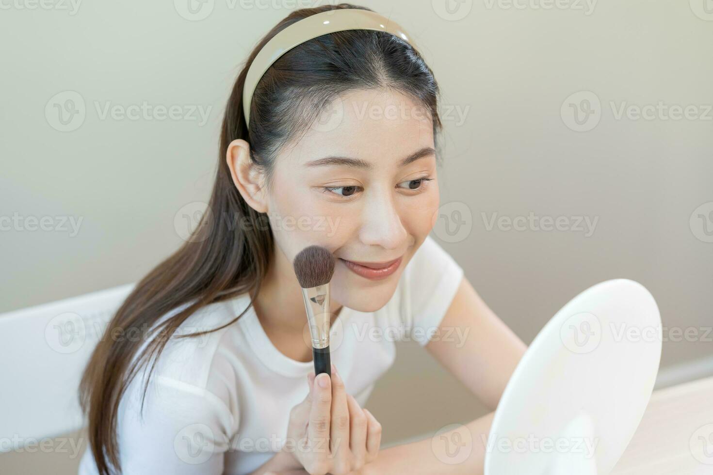 glücklich Routine Schönheit Konzept, ziemlich asiatisch jung Frau, Mädchen machen oben Gesicht durch bewirbt sich Pulver Stiftung durch Bürste um Gesicht, suchen beim das Spiegel beim heim. weiblich aussehen mit natürlich Mode Stil. foto