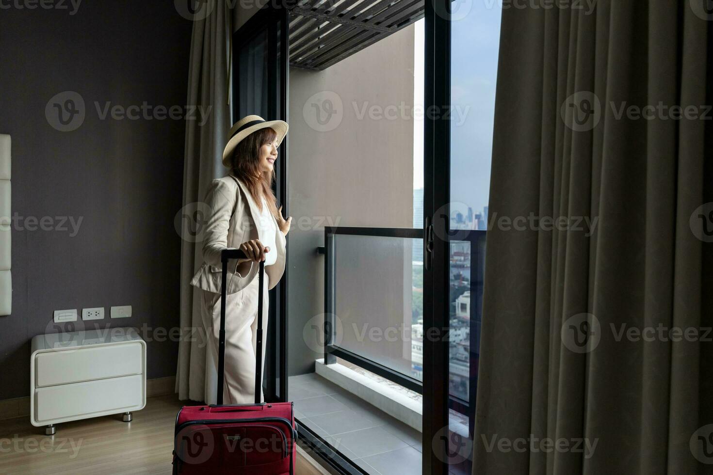 asiatisch Frau ziehen um das Luxus Hotel mit Gepäck auf ihr Ferien während suchen beim das Aussicht von Fenster mit hoch erhebt euch Gebäude im das städtisch Innenstadt Bereich zum Geschäft Ausflug und Eigentumswohnung Leben Verwendungszweck foto