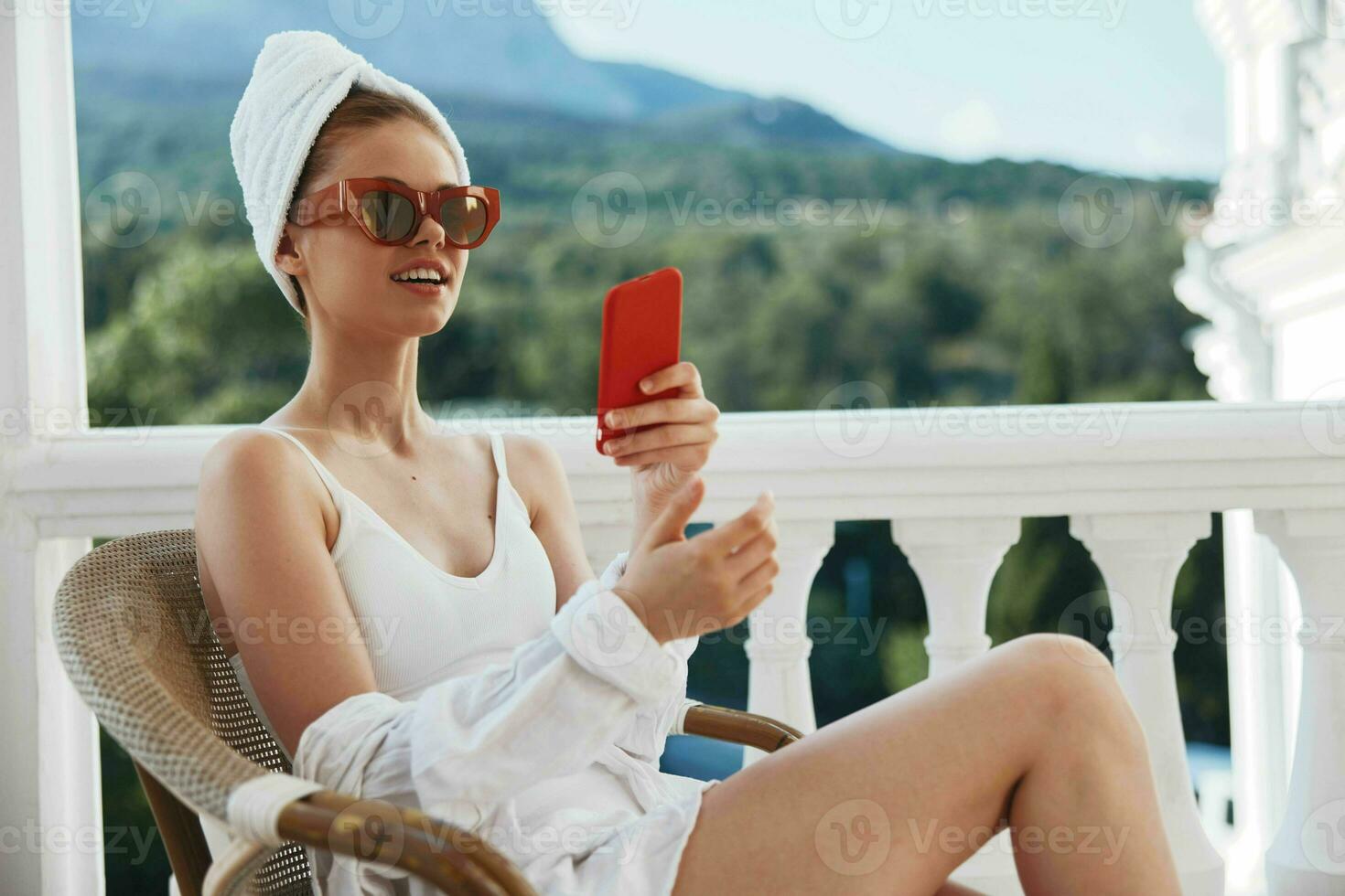 attraktiv jung Frau genießen das Morgen auf das Balkon suchen beim das Handy, Mobiltelefon Telefon Bildschirm Berg Aussicht foto