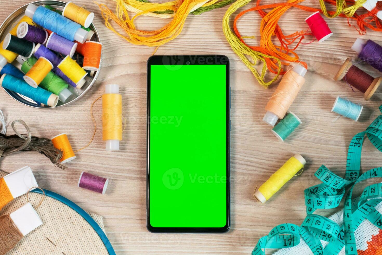 Smartphone mit ein Grün Bildschirm, Chroma Schlüssel Attrappe, Lehrmodell, Simulation zum das Anwendung. Konzept von Handarbeit, Nähen oder Stickerei mit Fäden. Hintergrund mit farbig Fäden. foto
