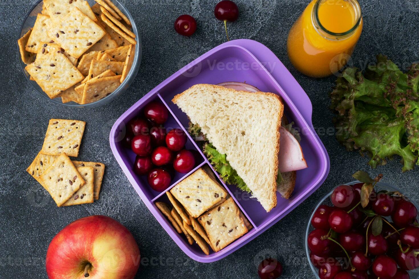 leckeres gesundes Sandwich in einer Brotdose, Keksen und Kirschen. Mittagessen mit in die Schule oder ins Büro nehmen. Saft in einer Flasche und einem Apfel. foto