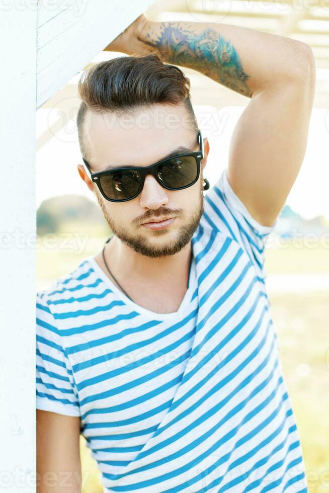 gut aussehend Hipster Mann im Sonnenbrille mit ein tätowieren auf das Strand auf ein sonnig Tag foto