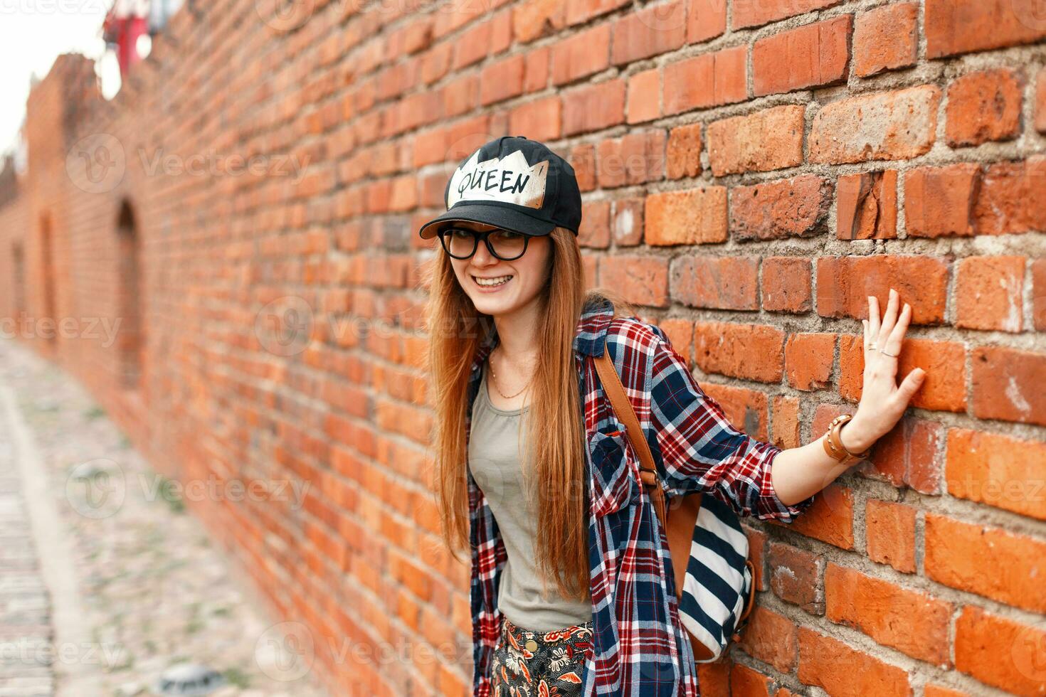 schön heiter Mädchen Hipster lächelnd im Hemd mit Brille in der Nähe von ein Backstein Mauer foto