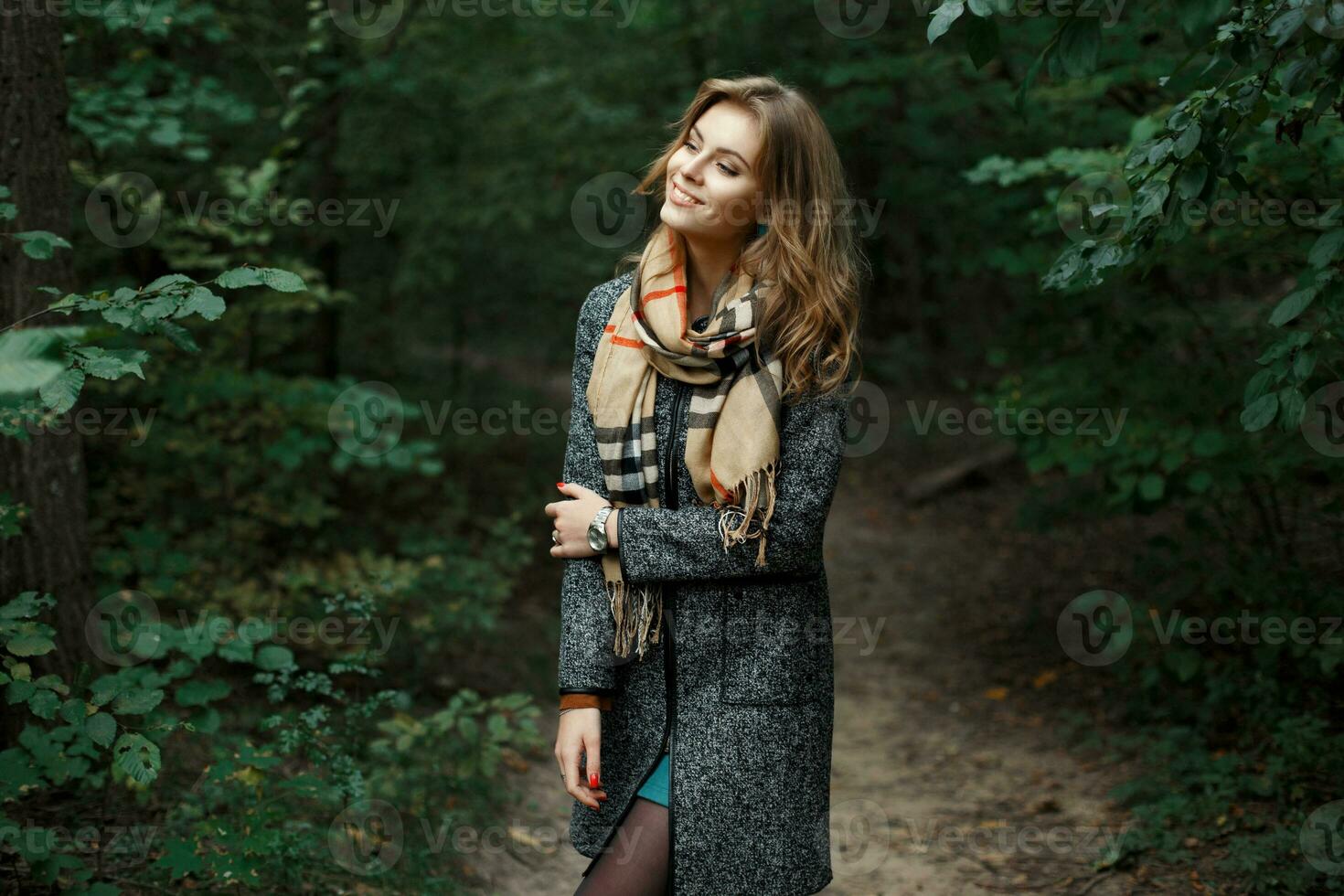 Mädchen im Mantel mit ein Schal im das Park auf ein Hintergrund von Gebüsch. foto