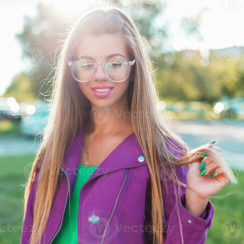 schön heiter Mädchen mit ein Süss Lächeln im Sonnenbrille und ein hell bunt Jacke auf ein sonnig Tag. foto