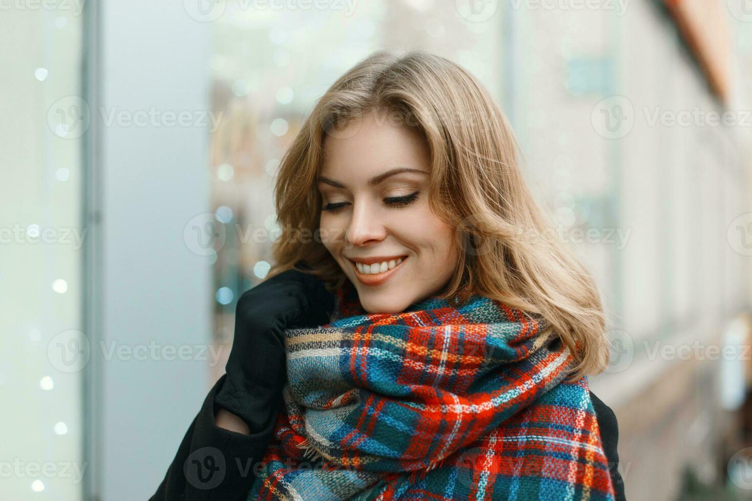 jung schön Mädchen mit ein Lächeln im Jahrgang Schal und schwarz Mantel auf das Hintergrund von Geschäft Fenster foto