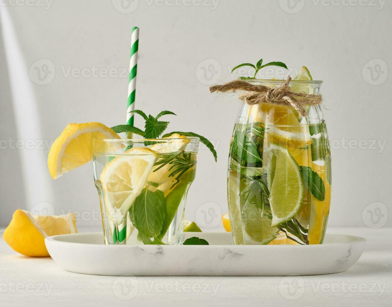 Limonade im ein transparent Glas mit Zitrone, Kalk, Rosmarin Zweige und Minze Blätter auf ein Weiß Hintergrund foto