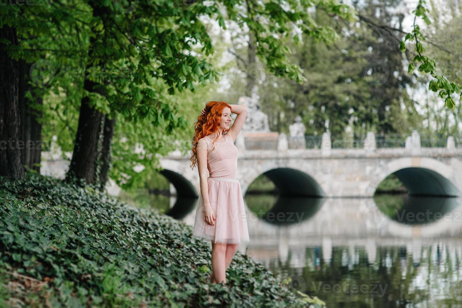 rothaariges junges Mädchen, das in einem Park zwischen Bäumen geht foto