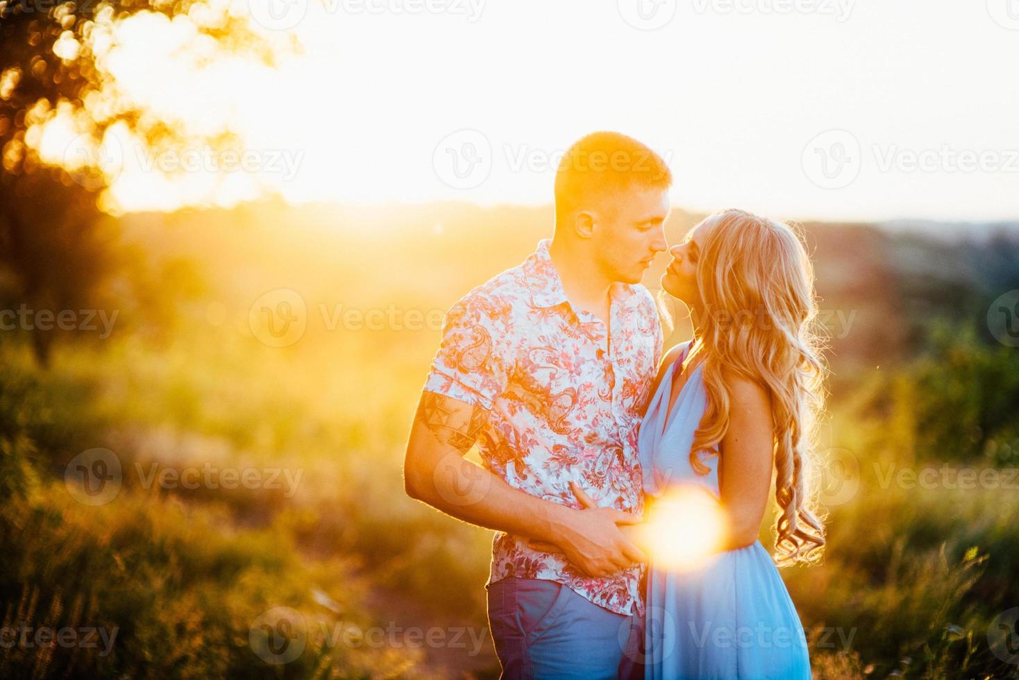 blondes Mädchen mit losen Haaren in einem hellblauen Kleid und einem Mann im Licht des Sonnenuntergangs foto