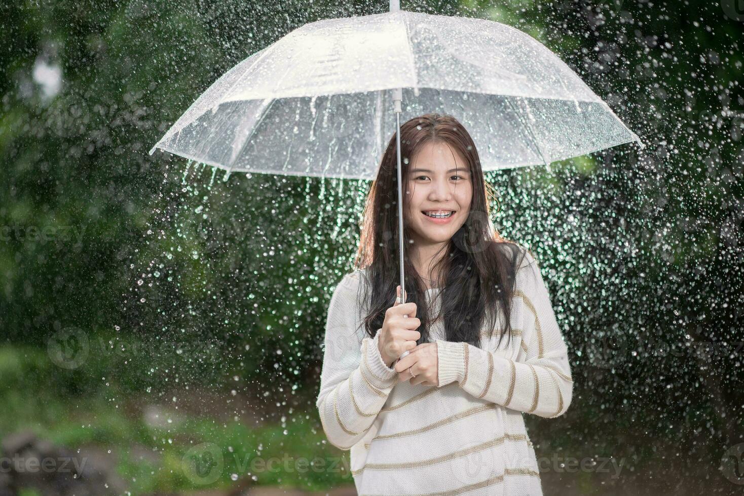 glücklich asiatisch Mädchen mit transparent Regenschirm unter das Regen foto