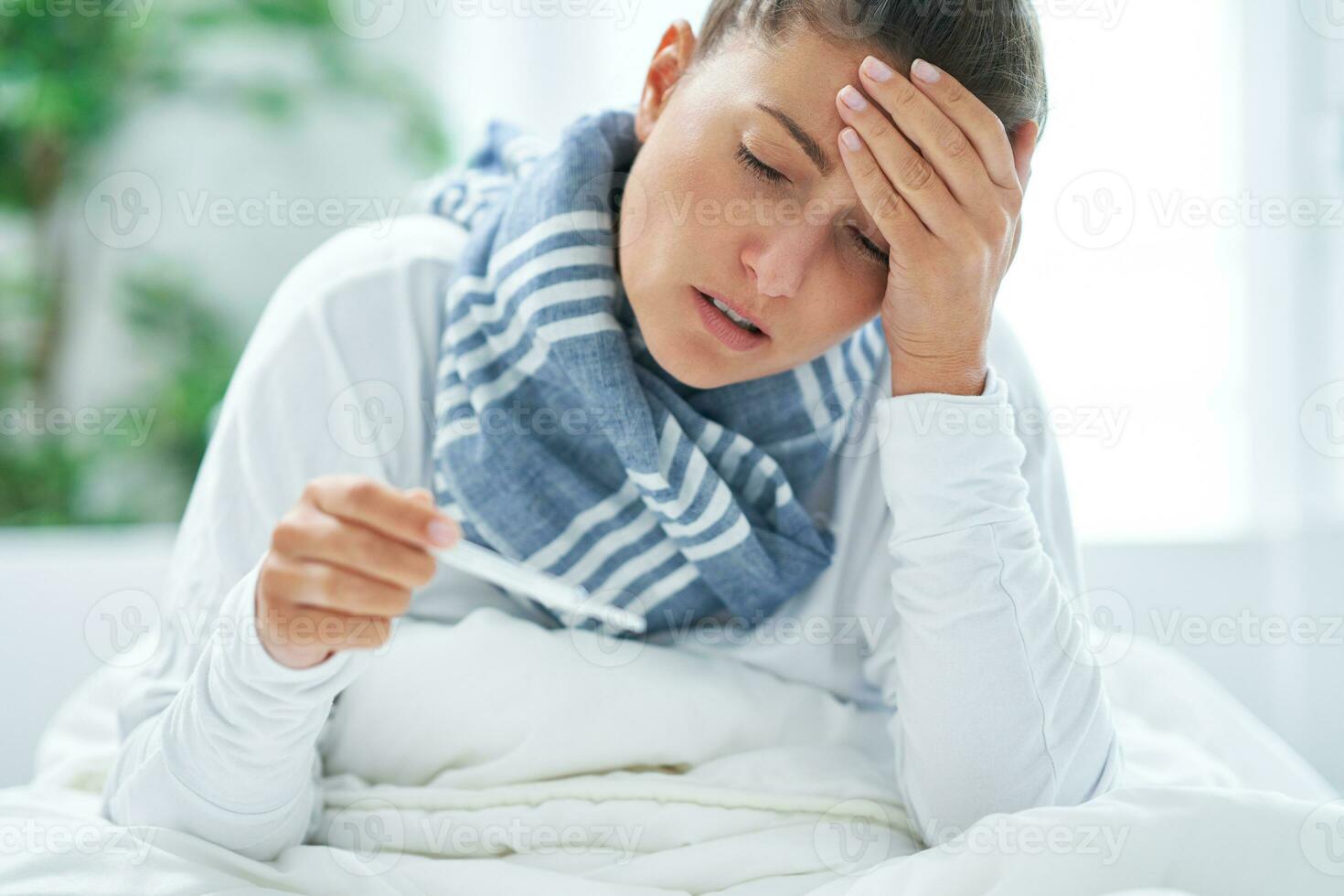 jung brünett Frau krank im das Bett mit Thermometer foto