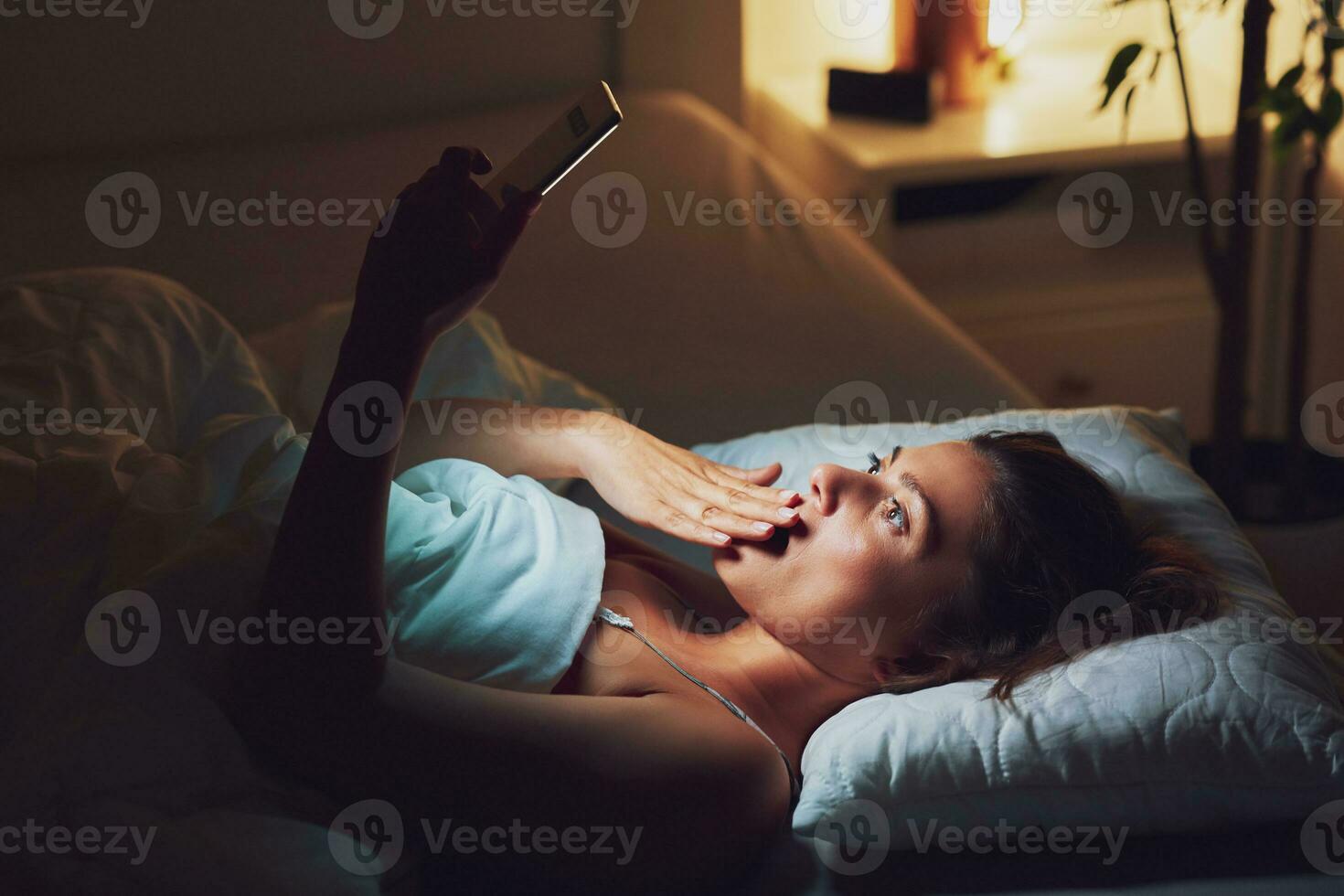 Frau beim Nacht im Bett mit Telefon foto