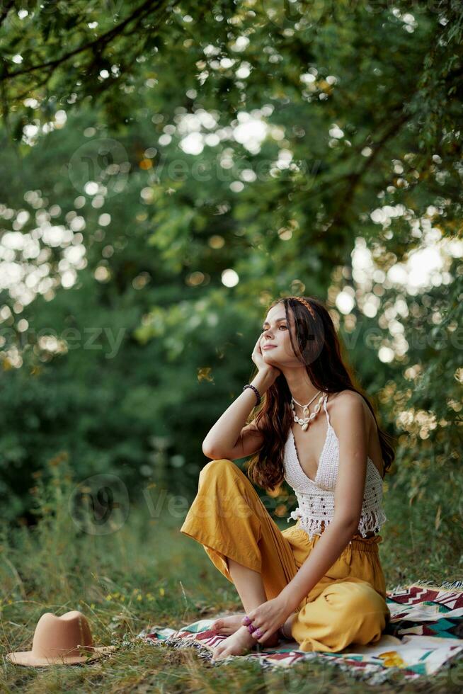 ein jung Hippie Frau meditiert im Natur im das Park, Sitzung im ein Lotus Position auf ihr bunt Plaid und genießen Harmonie mit das Welt im Öko-Kleidung im das Herbst foto