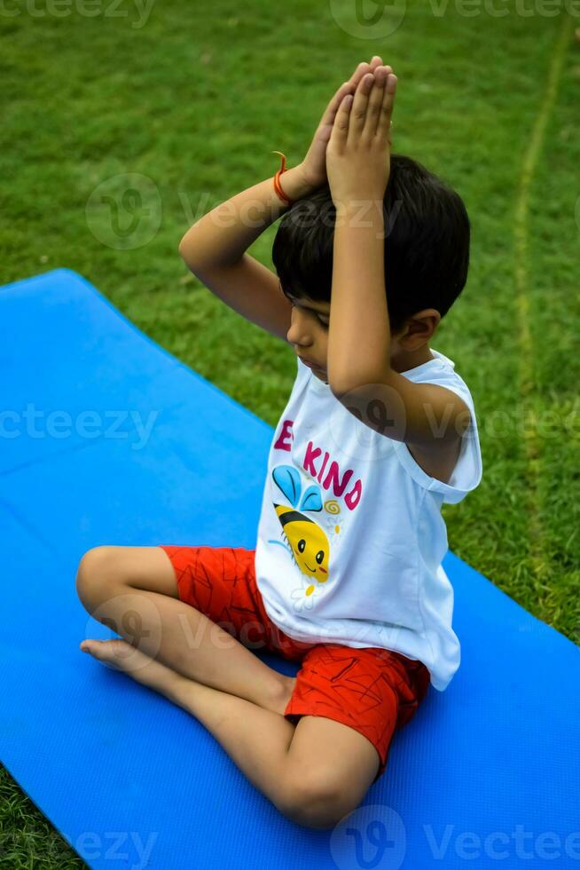 asiatisch Clever Kind tun Yoga Pose im das Gesellschaft Park draussen, Kinder- Yoga Pose. das wenig Junge tun Yoga und Meditation Übung. foto