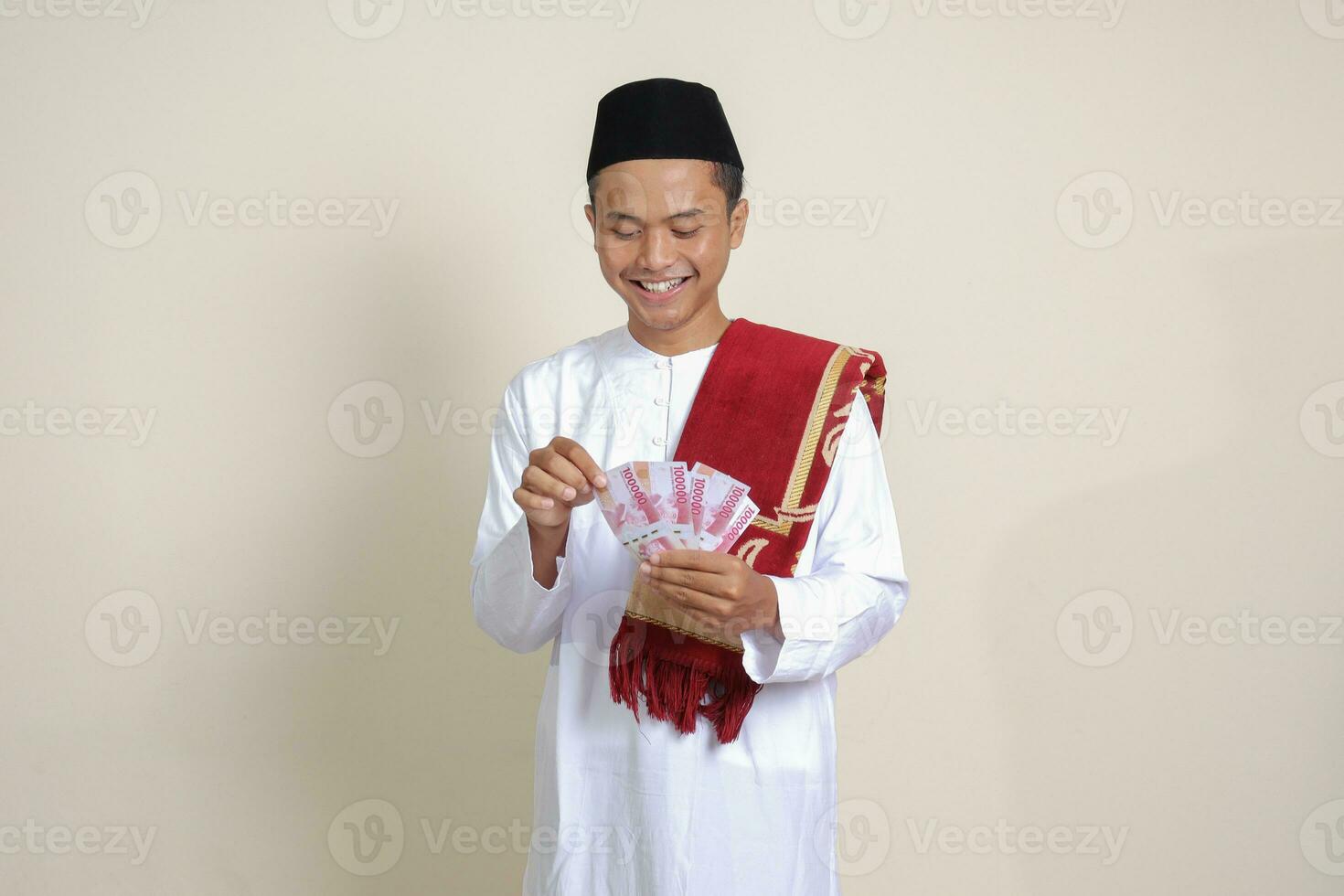 Porträt von attraktiv asiatisch Muslim Mann im Weiß Hemd zeigen einer hundert tausend Rupiah. finanziell und Ersparnisse Konzept. isoliert Bild auf grau Hintergrund foto