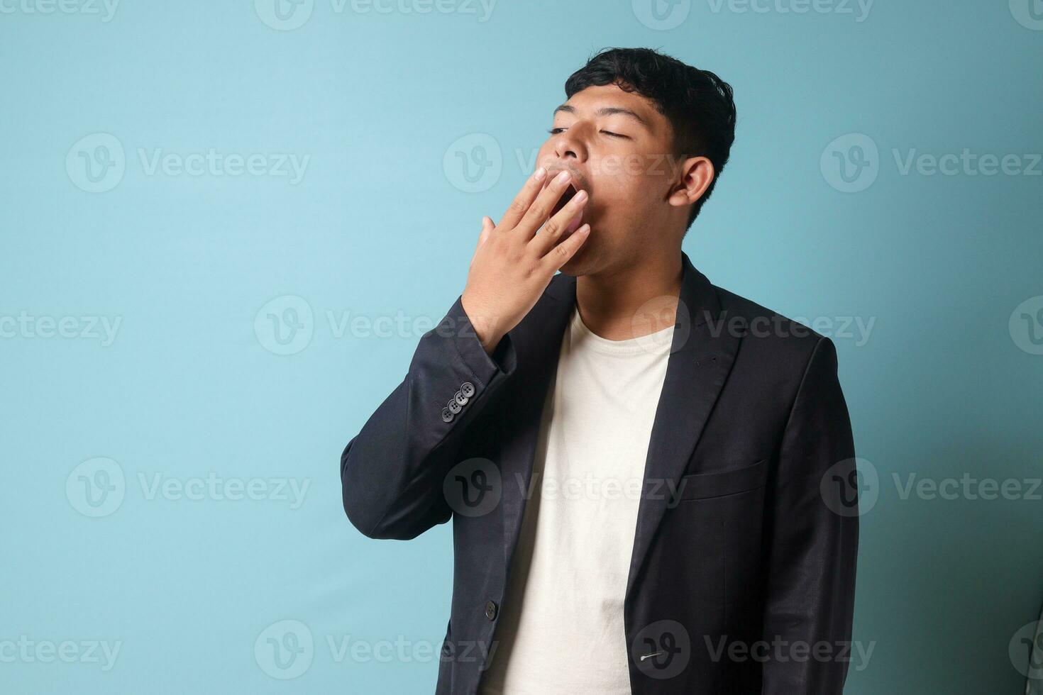 Porträt von jung asiatisch Geschäft Mann im beiläufig passen Gähnen im gelangweilt Ausdrücke. isoliert Bild auf Blau Hintergrund foto