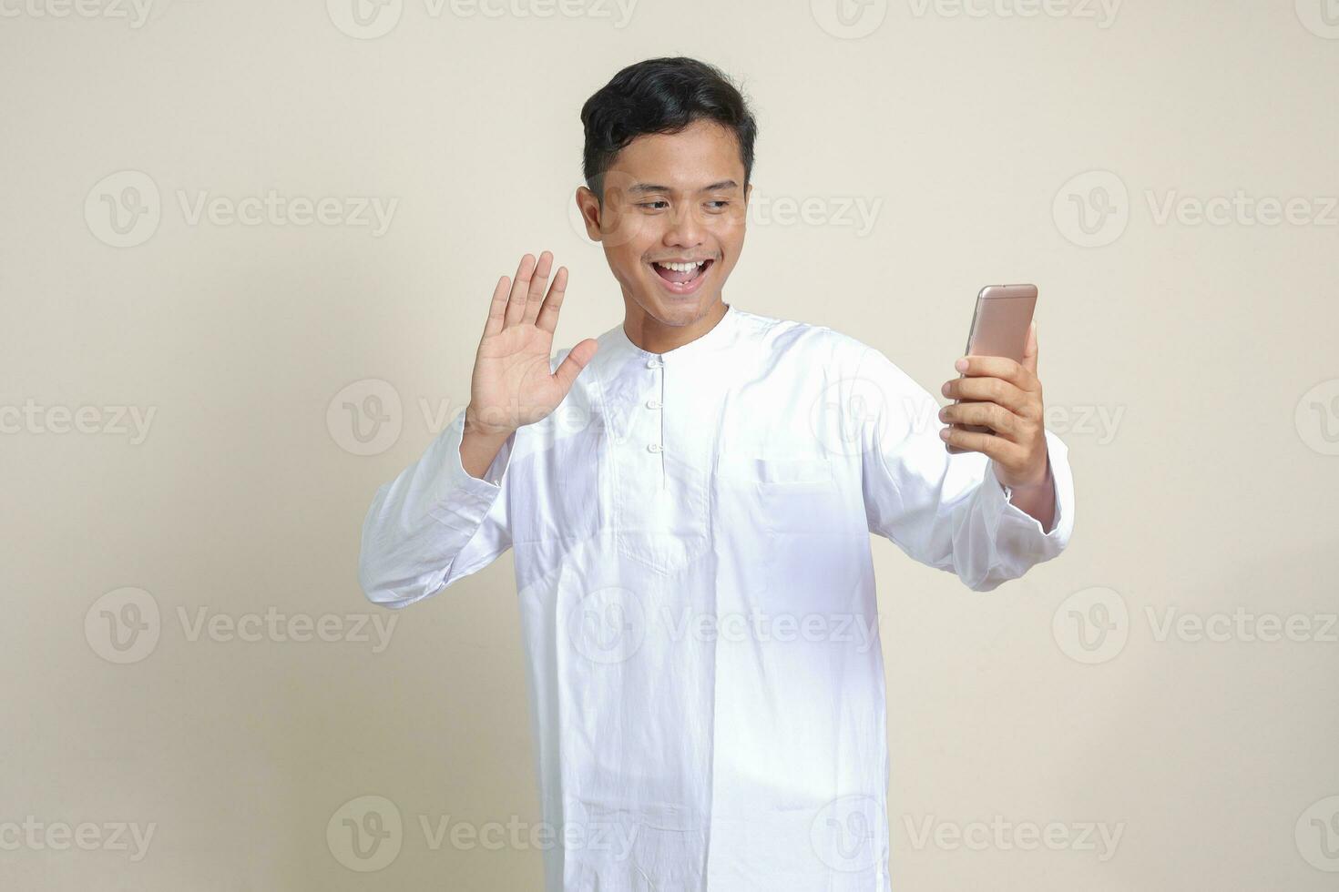 Porträt von attraktiv asiatisch Muslim Mann im Weiß Hemd nehmen Bild von selbst oder Selfie, Sprichwort Hallo und winken seine Hand während Video Forderung. isoliert Bild auf grau Hintergrund foto