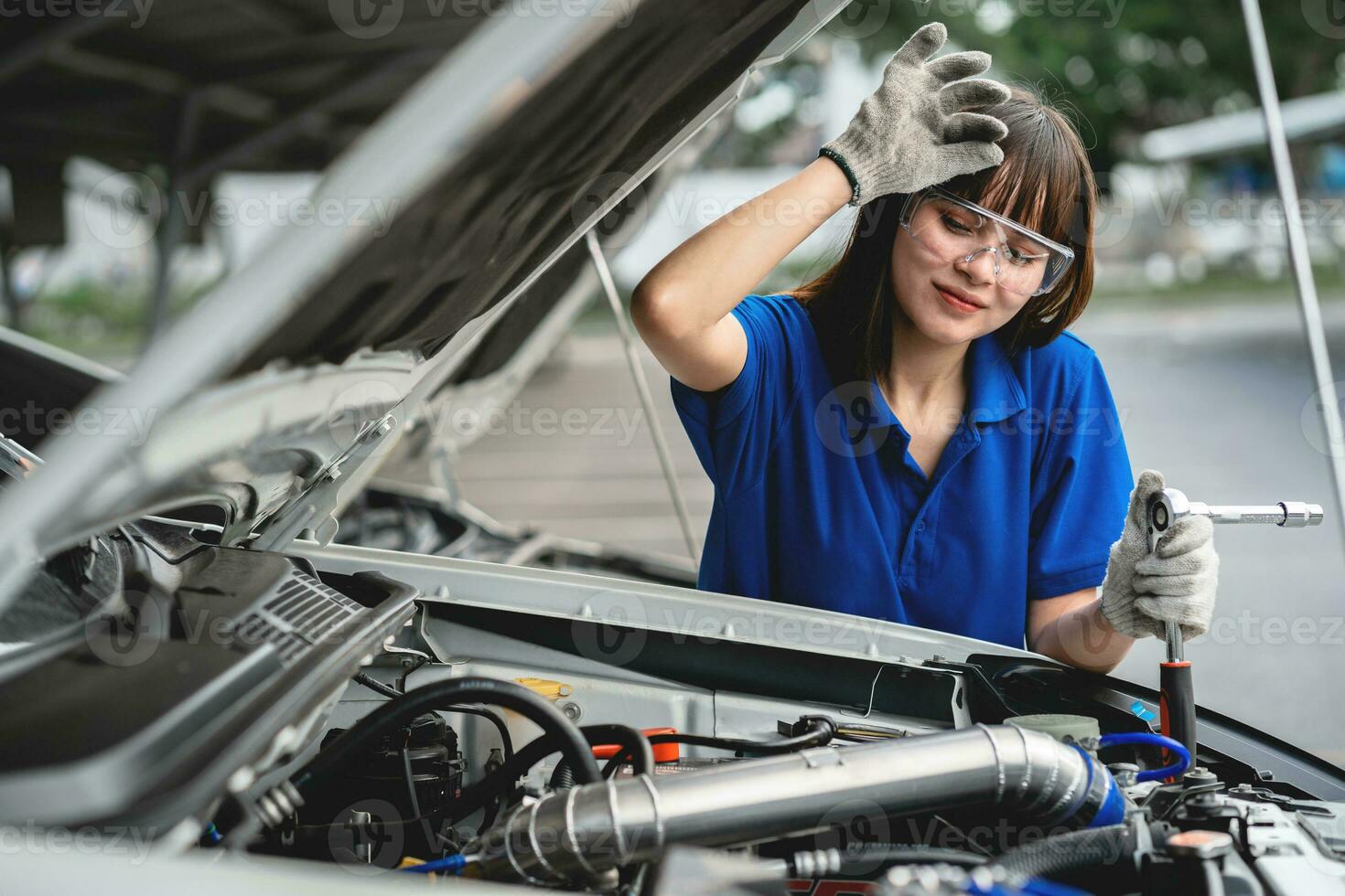 weiblich Mechaniker Arbeiten im ein Auto Service. ein Frau tragen Handschuhe und mit ein Rad unter ein Werkstatt Wagen. Reparatur Bedienung Konzept Auto Reparatur und Wartung. foto