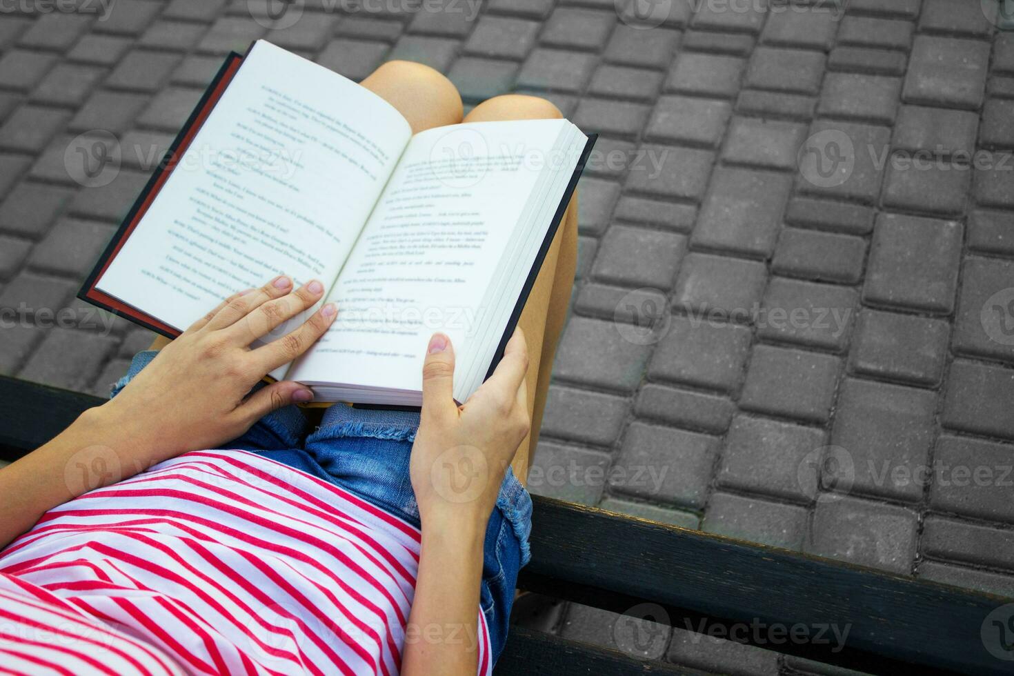 oben Aussicht von ein jung Mädchen lesen ein Buch. das Mädchen ist Sitzung auf ein Park Bank und lesen ein Buch. foto