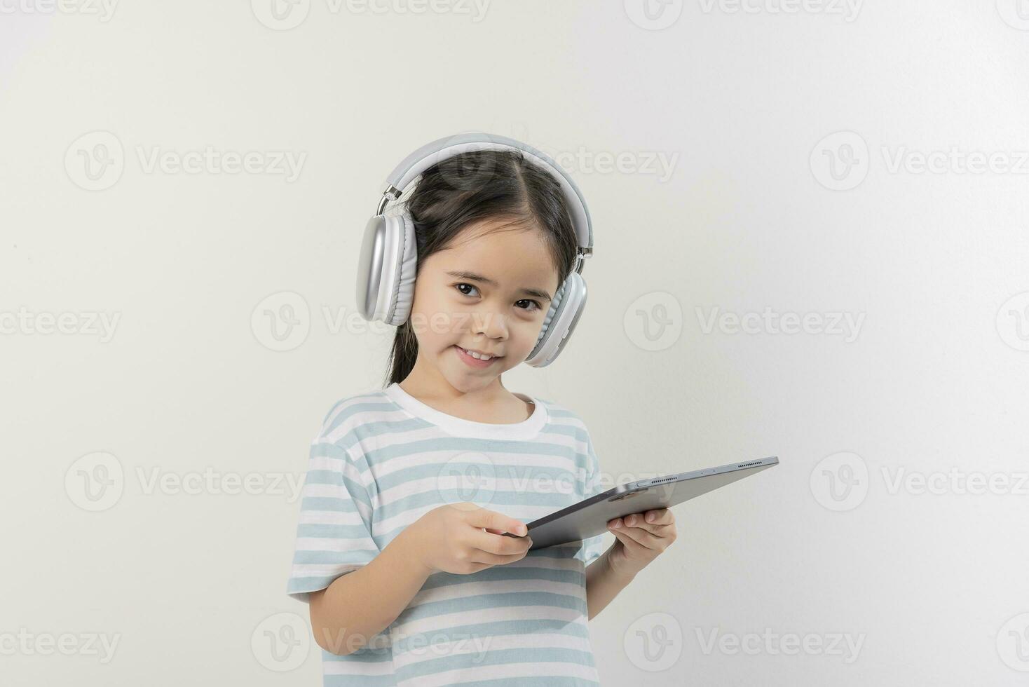 lächelnd wenig Mädchen stiting und halten ein Tablette mit Kopfhörer foto