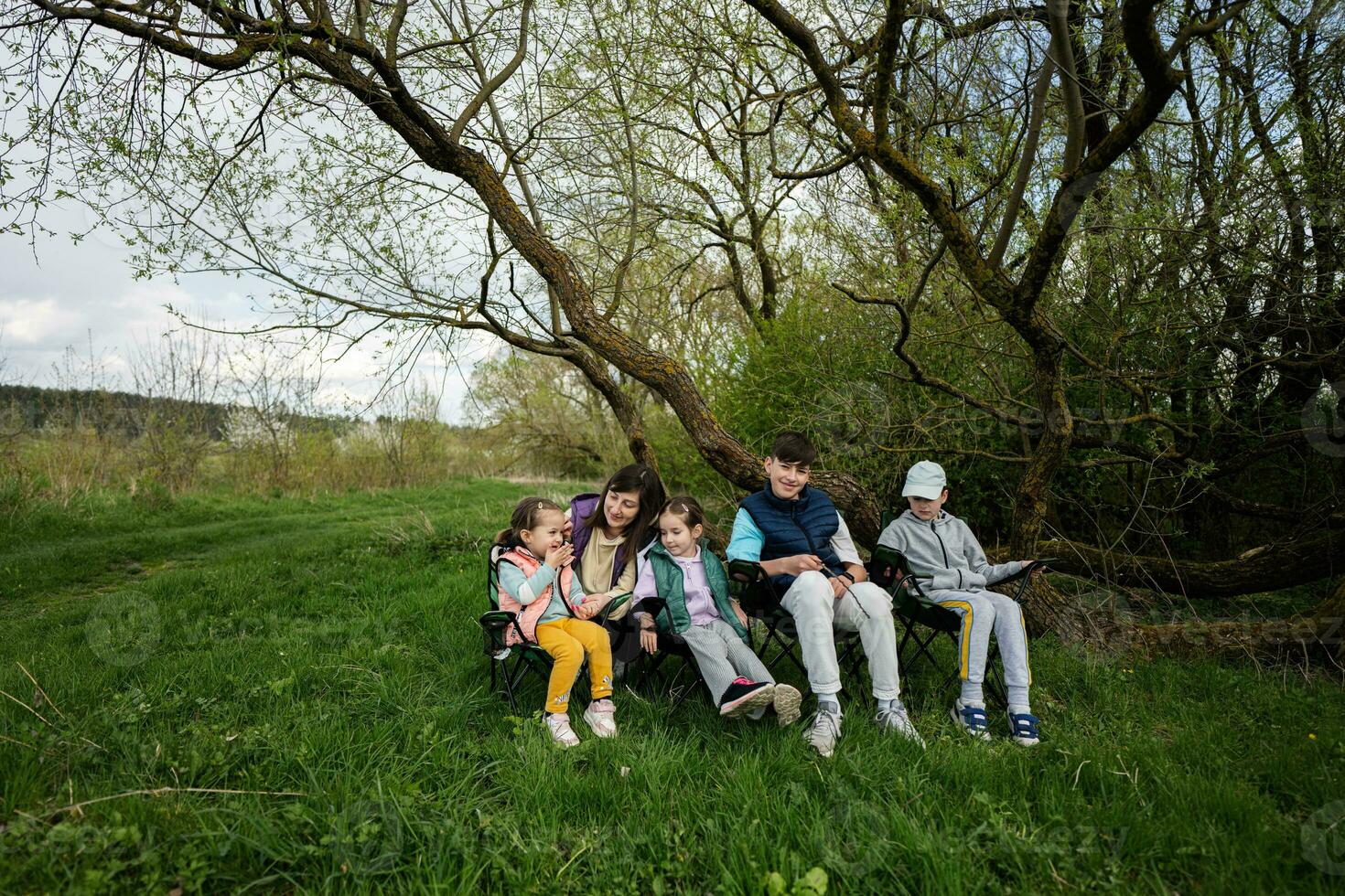 Mutter mit vier Kinder Sitzung auf Stühle beim Frühling Wald. foto