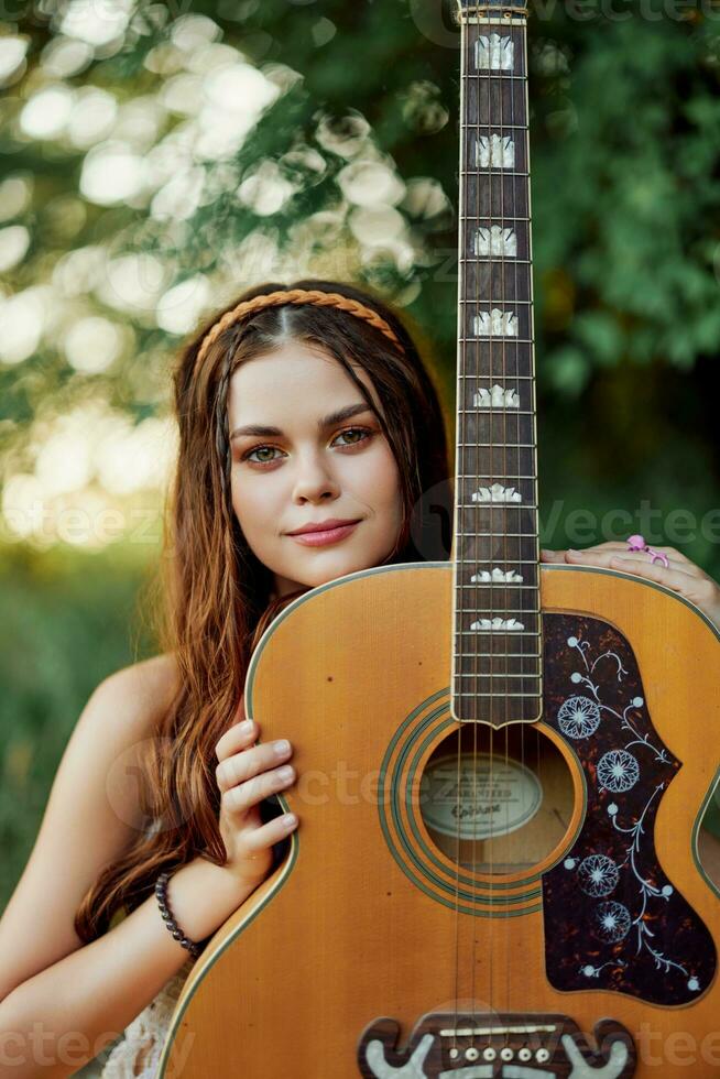 jung Hippie Frau mit Öko Bild lächelnd und suchen in das Kamera mit Gitarre im Hand im Natur auf ein Ausflug foto